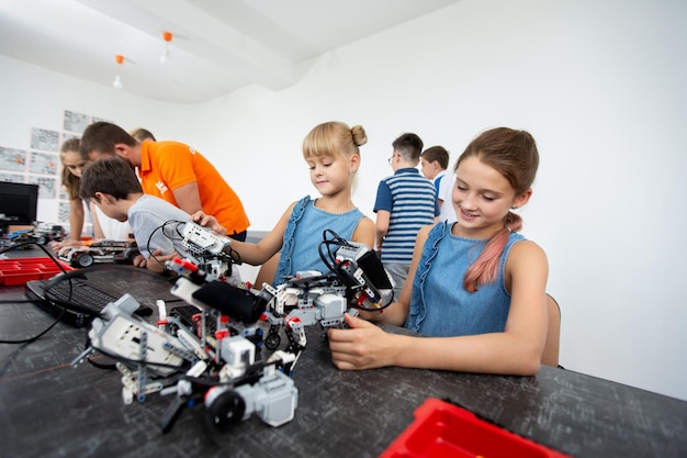 Education, children, technology, science and people concept - group of happy kids with laptop computer building robots at robotics school lesson
