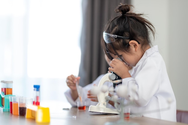 Education, science, chemistry and children concept - kids or students with test tube making experiment at school laboratory
