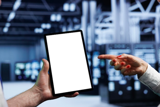 Elderly programmers in high tech workspace using mock up tablet to set up configuration management tools that enable automatic failover, preventing server cabinets system crash, close up