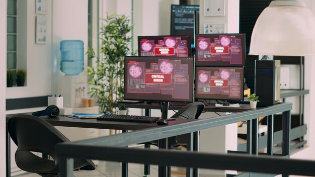 Empty agency office with multiple monitors showing system crash warning on display, critical error message flashing on screen. Computers displaying security breach malfunction at desk.