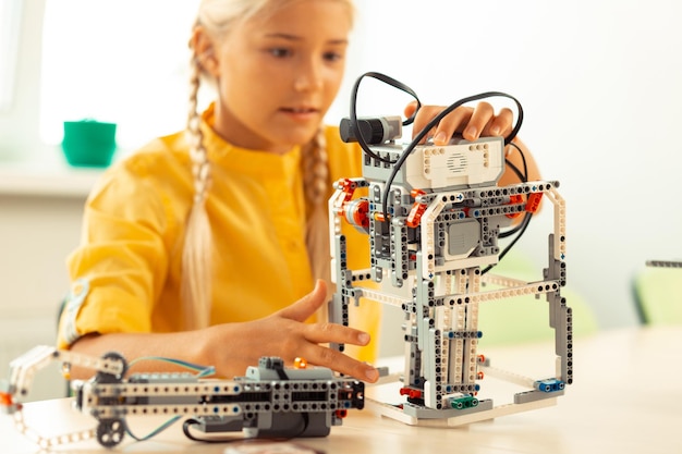 enthusiastic girl sitting at the school desk and building a robot using construction set during her science lesson