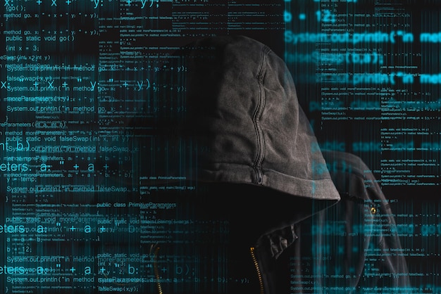 faceless hooded anonymous computer hacker with programming code from monitor deep web hacking and ransomware concept
