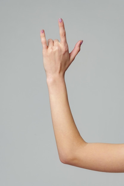female hand gesturing rock sign on gray background