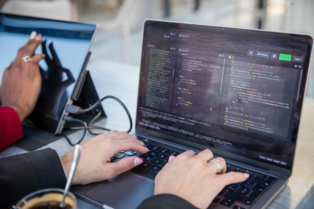 Female programmer writes some code and drinks coffee while sitting near her colleague