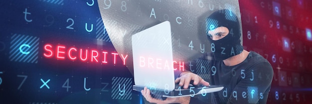 Focused burglar with balaclava holding laptop against digitally generated french national flag