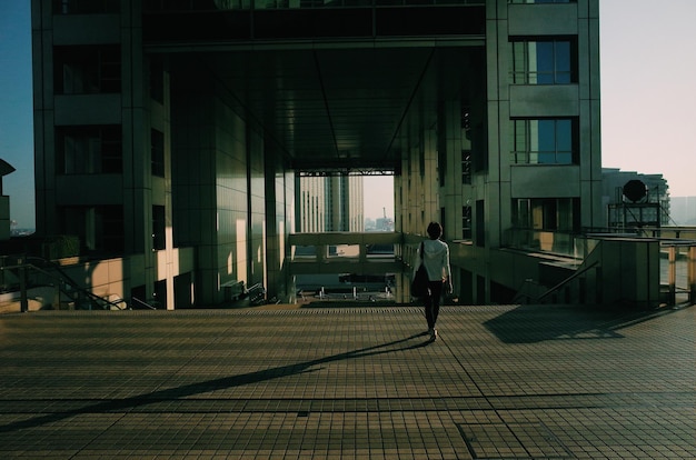 full length rear view of woman walking towards building on sunny day