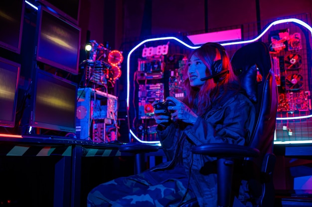 Gamer using joystick controller for virtual tournament plays online video game with computer neon lights woman wear gaming headphones playing live stream esports games console gaming room