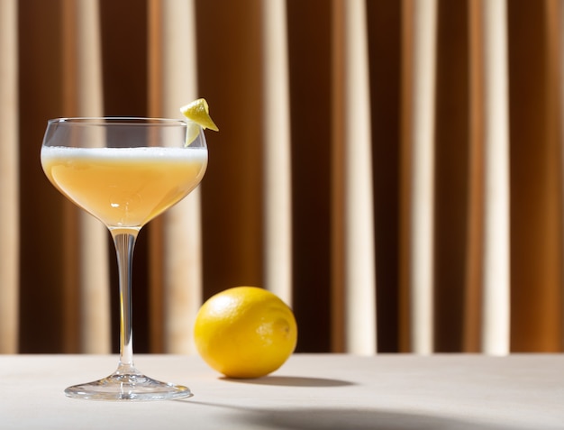 Glass filled with whiskey sour cocktail with lemon on the table