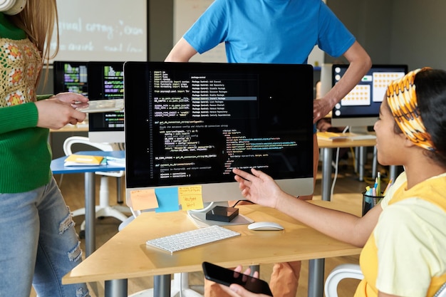 Group of students discussing computer codes on computer in team during IT lesson