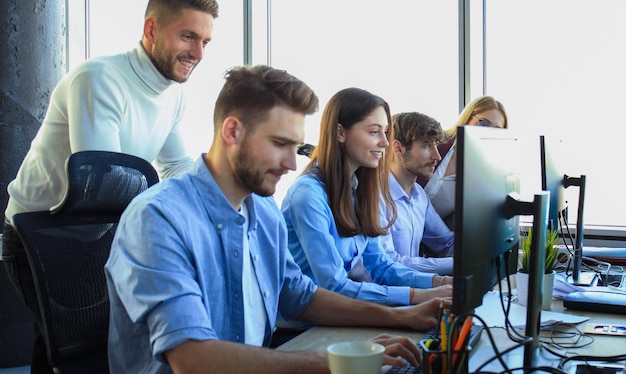 Group of young people in casual wear sitting at the office desk and discussing something while looking at PC together