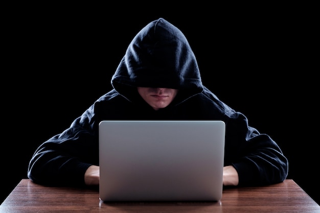 hacker in a dark hoody sitting in front of a notebook