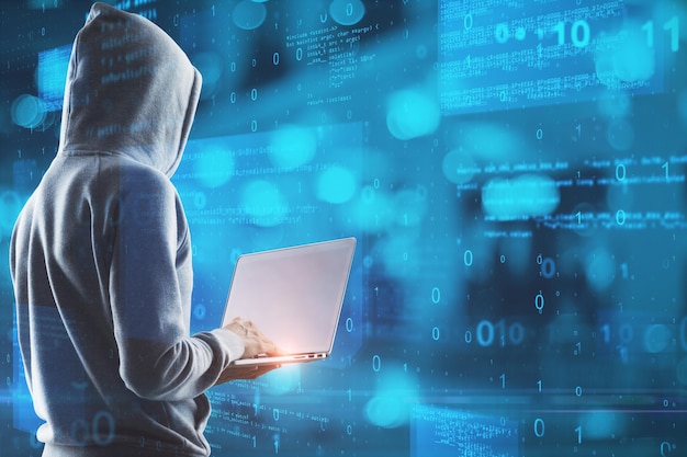 hacker in hoodie using laptop with abstract glowing blue coding background binary code theft technology data and internet concept double exposure