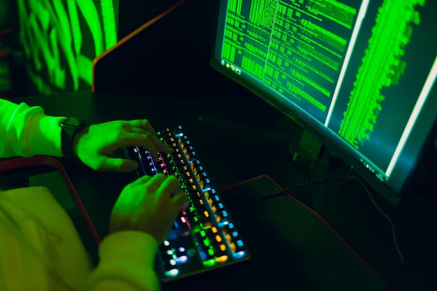 Hacker using computer malware software and hacking binary code green digital interface hands keyboard close up