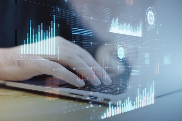 Hands typing on laptop with virtual financial statistics on blue screen
