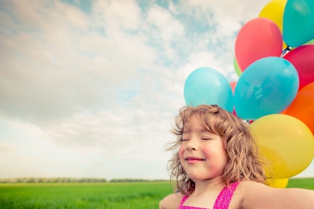 happy child playing with colorful toy balloons outdoors smiling kid having fun in green spring field against blue sky freedom concept