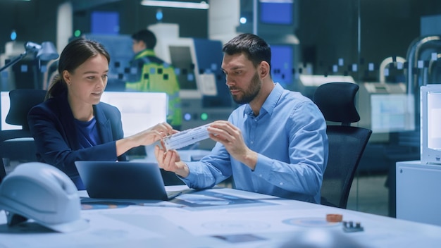 Industry 40 Modern Factory Meeting Room Chief Engineer Holds Mechanism Shows it to Female Designer They Talk Scientists in Contemporary Lab Build Electronic Machinery for With Futuristic Design