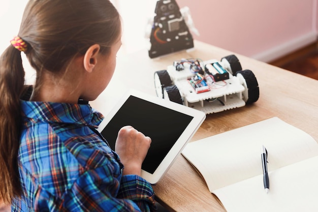 inventions and creativity. teenager schoolgirl programming the contoller of robot car with digital tablet, back view. gadgets, e-learning, modern teaching technology, stem education.