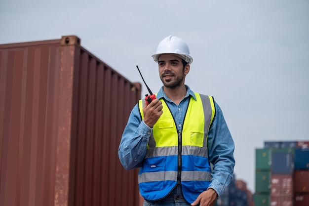 logistic manager talking on the walkietalkie at container warehouse for control loading containers in container yard terminal shipping worker container talking radio to manage the export of goods