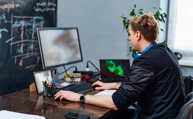 male programmer working on desktop computer near monitor at office in software development company website design programming and coding technologies