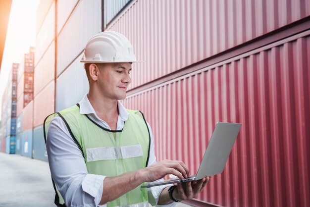 Man using laptop while standing against cargo containers at dock