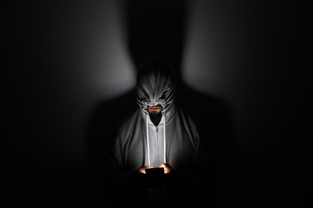 man wearing hooded shirt using mobile phone against wall