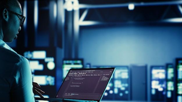 Manager overseeing data center running code on laptop troubleshooting and upgrading technologically advanced infrastructure designed to accommodate servers networking systems and storage arrays