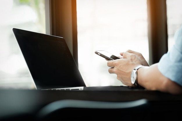 Midsection of businessman using mobile phone by laptop at table in office