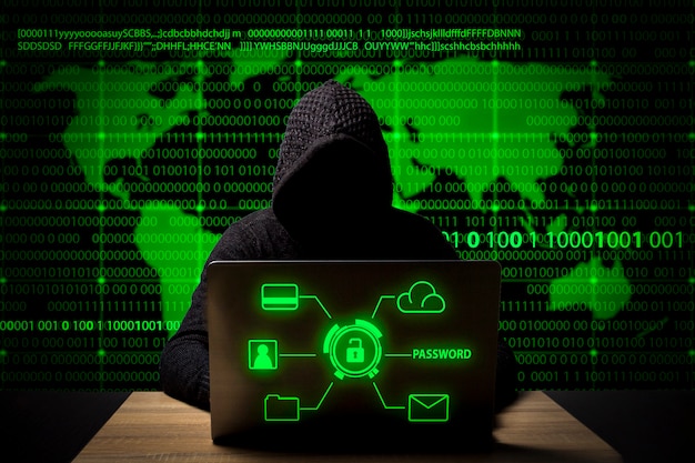 Một hacker mặc áo khoác có mũ trùm đầu và máy tính xách tay đang ngồi ở bàn