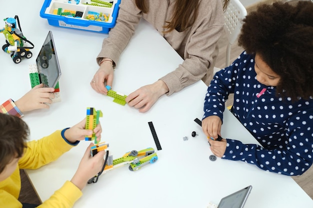 Multiethnic kids at stem lesson constructing robot in classroom with woman teacher children making