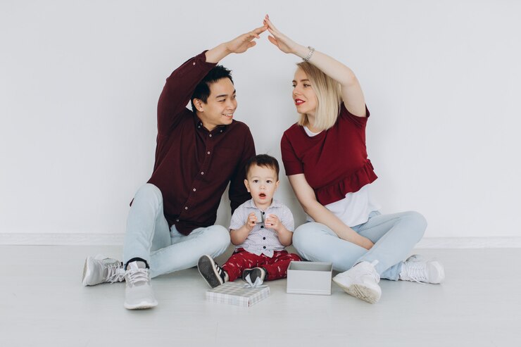 Photo new building residential house purchase apartment concept. multicultural family with son sitting on the floor, caucasian mom and asian dad making roof with hands arms over head