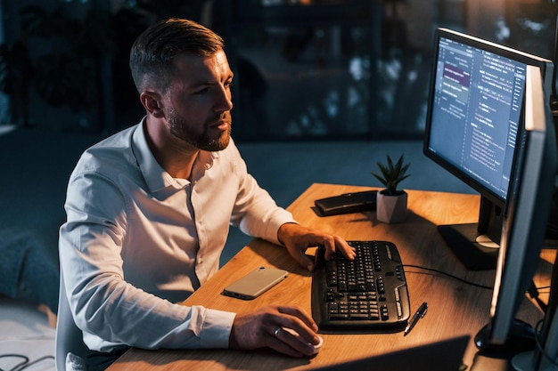 Night time Young businessman in formal clothes is in office with multiple screens