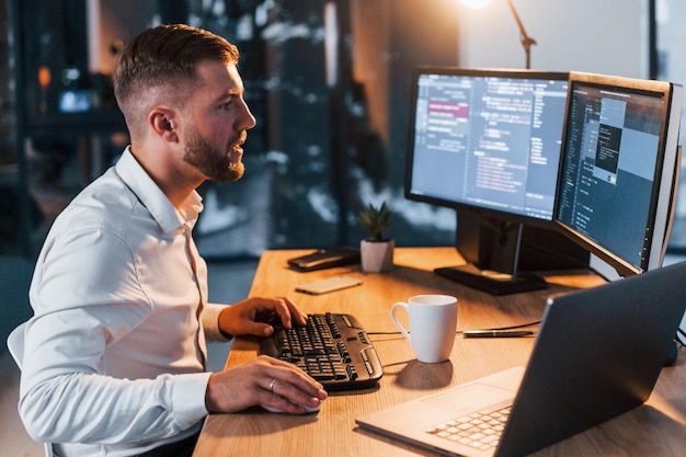 Night time Young businessman in formal clothes is in office with multiple screens