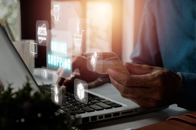 Online shopping concept Person hands holding credit card and using laptop with online shopping icon on virtual screen