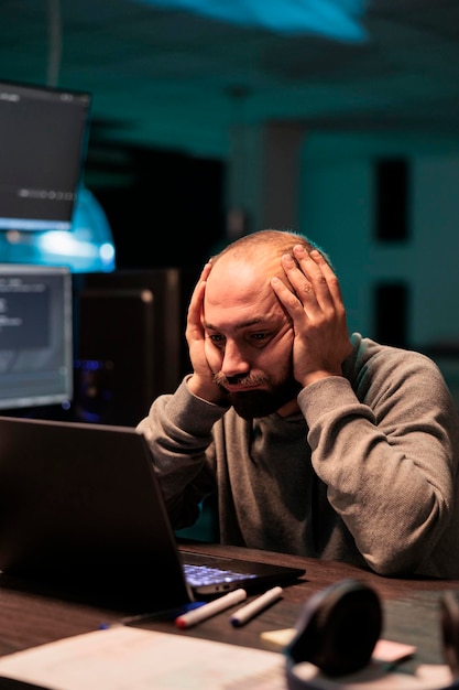 Overworked programmer working on app developing after hours, feeling tired and stressed about it failure. Sad frustrated coder programming source code late at night, exhausted man.