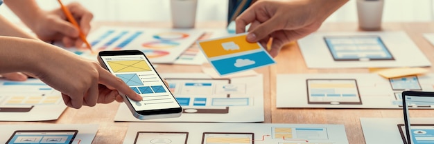 Panorama shot of frontend developer team brainstorming UI and UX designs for mobile app on paper wireframe interface User interface development team planning for userfriendly UI design Scrutinize