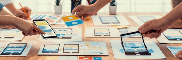 Panorama shot of frontend developer team brainstorming UI and UX designs for mobile app on paper wireframe interface User interface development team planning for userfriendly UI design Scrutinize