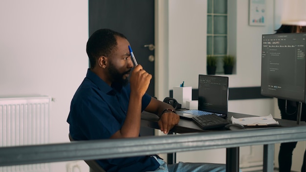 Pensive african american programer working on code development and brainstorming ideas to create html script. Software developer thinking about database server in it agency office.