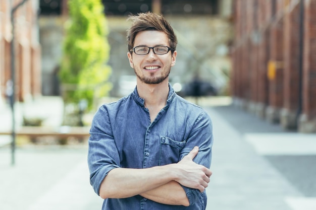 portrait of a young teacher on campus man with arms crossed smiling and looking at camera with beard and glasses