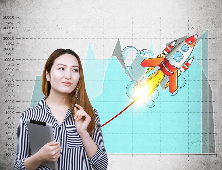Photo portrait of an asian businesswoman with a tablet computer standing near a concrete wall with a launching rocket and a blue graph on it.