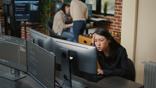 Portrait of asian programer focused on writing code encounters unexpected compiling error sitting at desk in software development office. Coder having system failure while creating algorithm.