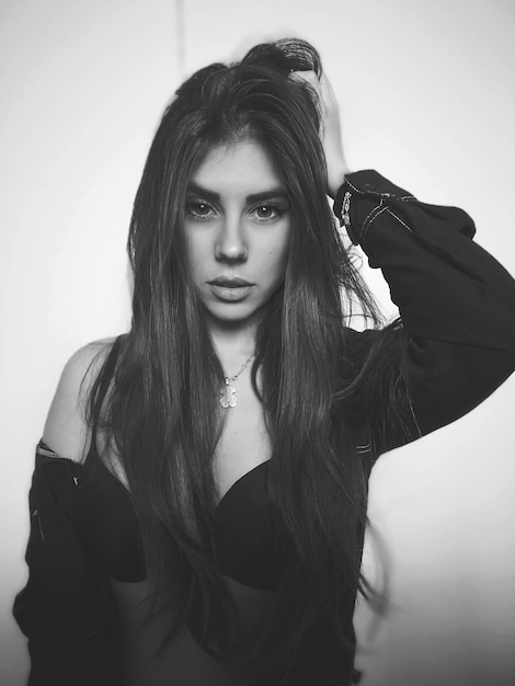 portrait of beautiful young woman with hand in hair standing against wall