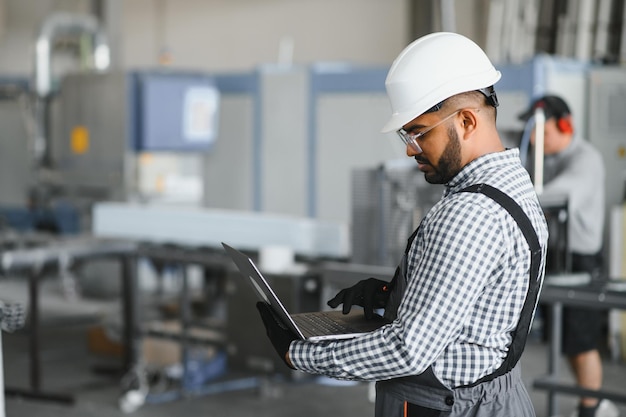 Portrait of Indian male engineer into the factory while his hand is holding the laptop