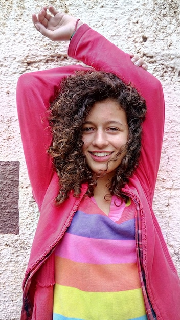 portrait of smiling girl with arms raised standing against wall