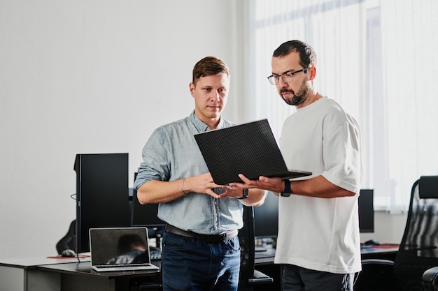 Portrait of two professional male programmers working on computer in diverse offices Modern IT technologies development of artificial intelligence programs applications and video games concept