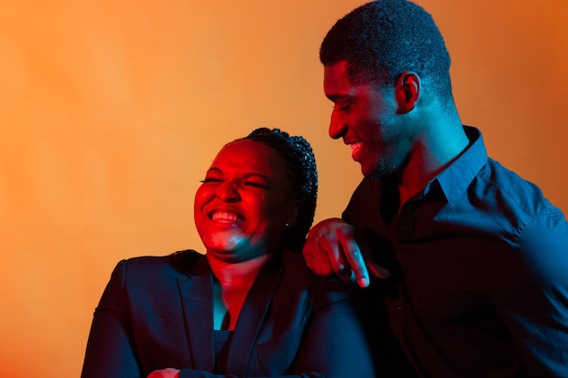 portrait of young african american couple in love posing at  dressed in classic clothes. neon