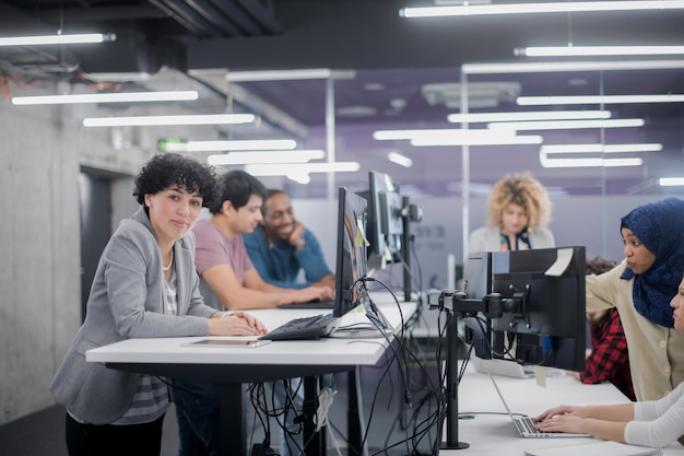 portrait of young female software developer at busy startup office with her multiethnic business team in background