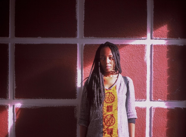 portrait of young woman with braided hair standing against window