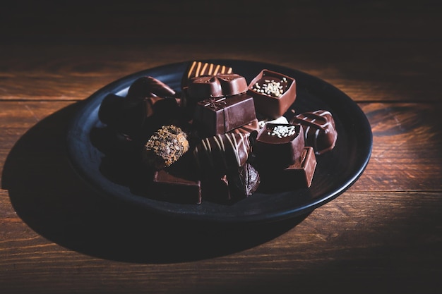 pralines on plate on wooden base deep shadows close up sweet and chocolate concept