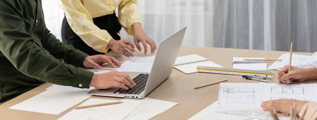 Professional architect edited blueprint by using laptop while project manager point the mistake point at meeting room on meeting table with architectural document scatter around Closeup Delineation
