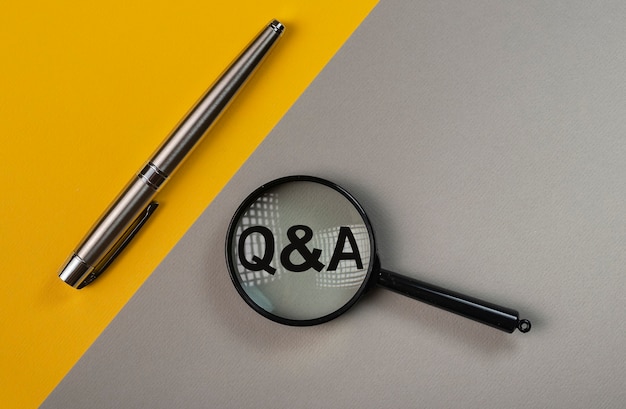 q or qa concept through magnifying glass on yellow and gray colored table.